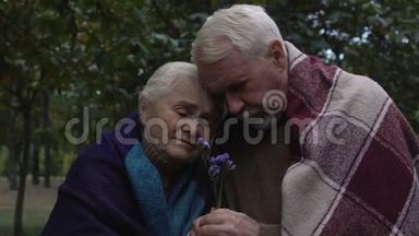 一对年迈的夫妇被格子包裹，抱着手里的花，悲伤
